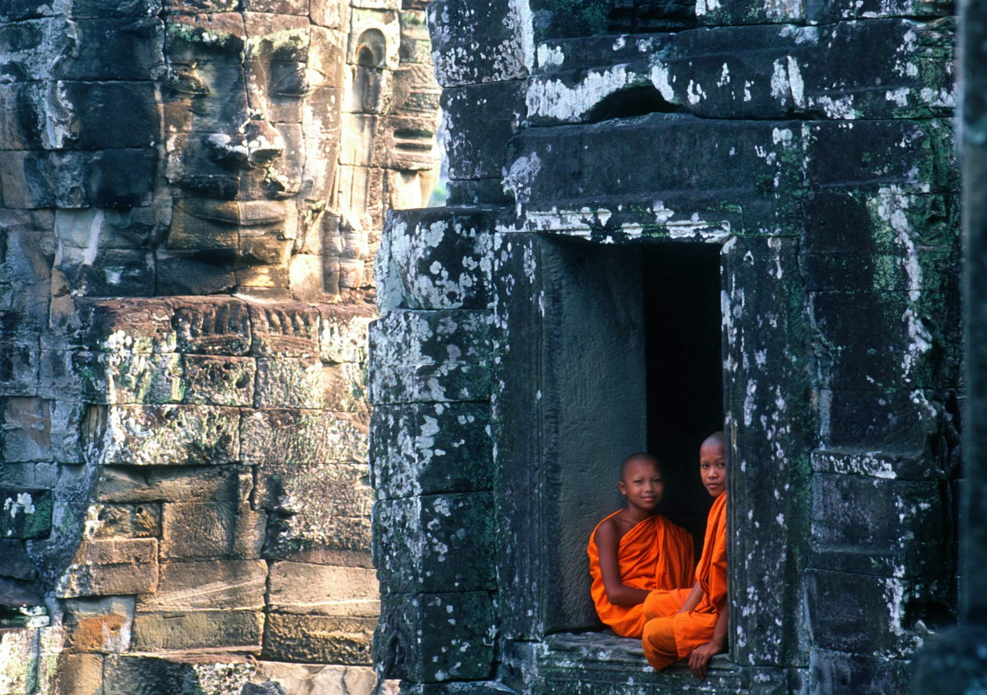 Two Cambodian monks in orange robes sit in a huge space in a wall in Angkor Wat