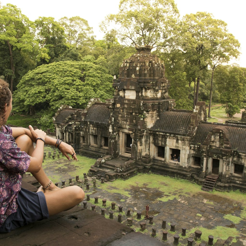 Young traveller, wearing a purple shirt and dark shorts, walking around the Baphuon temple, in Angkor Wat, during a cloudy day