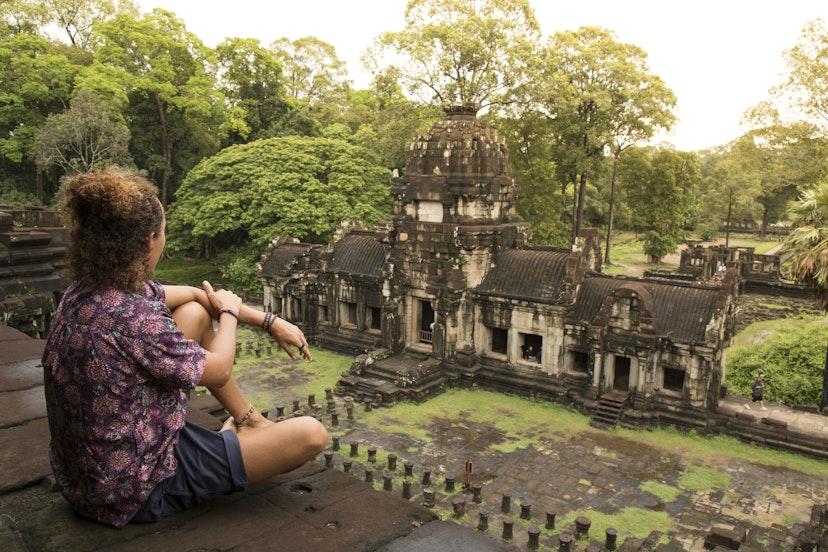 Young traveller, wearing a purple shirt and dark shorts, walking around the Baphuon temple, in Angkor Wat, during a cloudy day