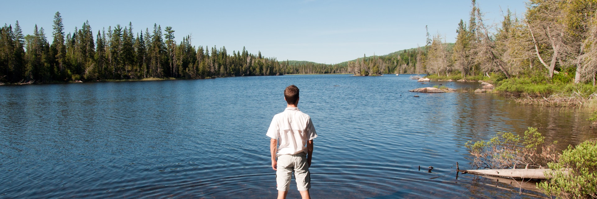 Man standing in water relaxing and contemplating wildness of lake superior provincial park, Canada.
