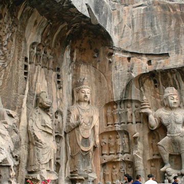 Luoyang, China - June 19, 2008: Tourists take photos in front of the massive stone carvings of Buddha at the Longmen Grottoes.
