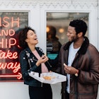 Mixed race couple on a day out at seaside having fun and laughing outside a fish and chip shop