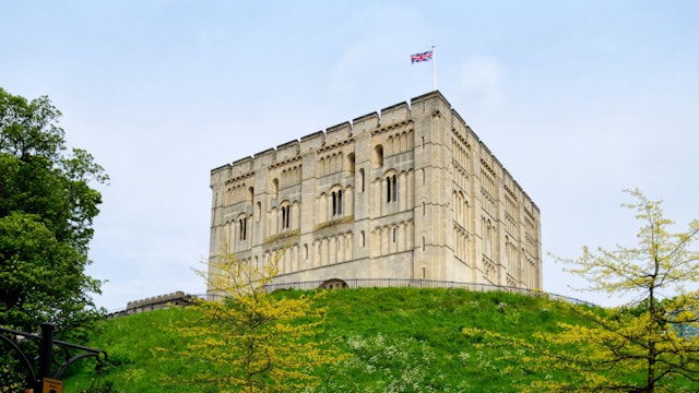 "Norwich, England - May 17, 2012: A man walking past Norwich Castle keep and castle mound on a spring day. The stone keep was constructed by order of the King between 1100 and 1120 to replace a wooden structure which stood on the same mound dating back to the Norman conquest of 1066. The castle was used as a prison until 1887 and has been used as a museum since 1894."