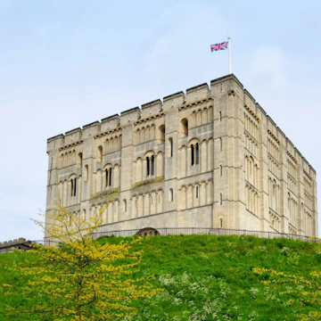 "Norwich, England - May 17, 2012: A man walking past Norwich Castle keep and castle mound on a spring day. The stone keep was constructed by order of the King between 1100 and 1120 to replace a wooden structure which stood on the same mound dating back to the Norman conquest of 1066. The castle was used as a prison until 1887 and has been used as a museum since 1894."