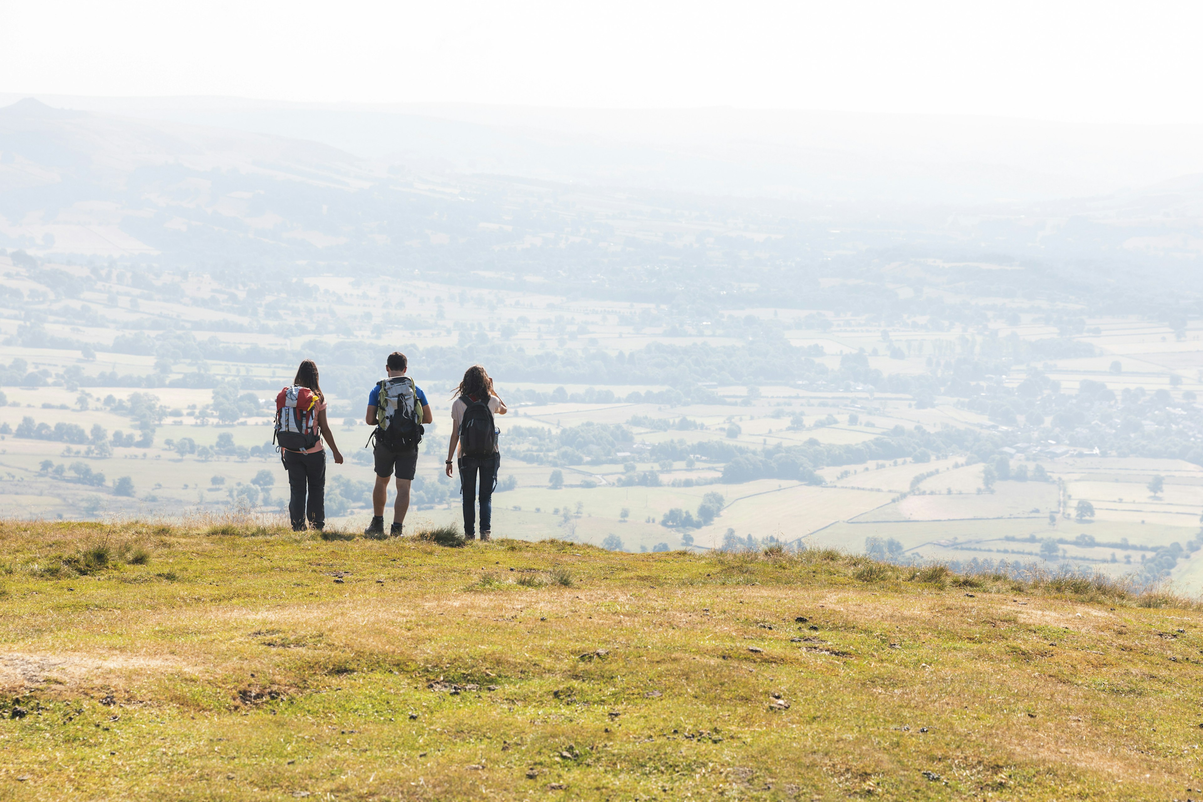 Three hiking friends stand on a cliff looking out over rolling countryside in the Peak District