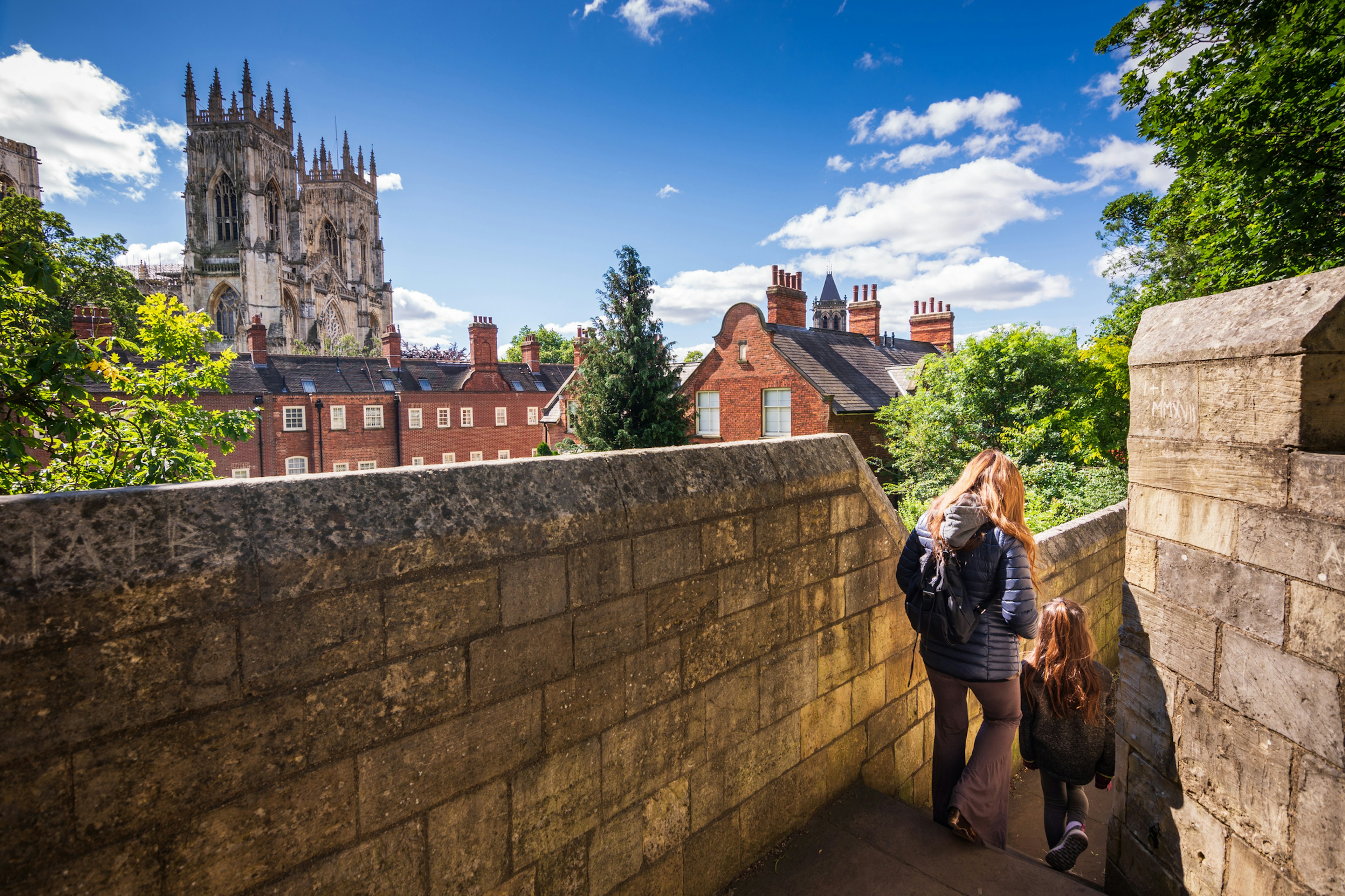 A mother and child walk along city walls in York. A large Gothic cathedral (York Minster) is in the background