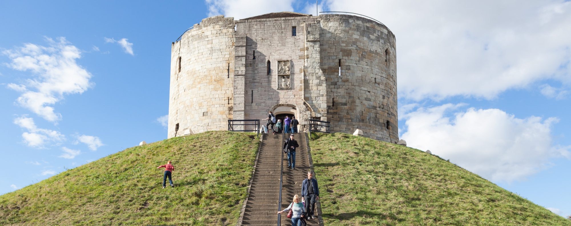 York, United Kingdom - October 2, 2016: View of Clifford's Tower, a Norman Motte and Bailey castle in York, England, with visitors climbing the steps to see the attraction.