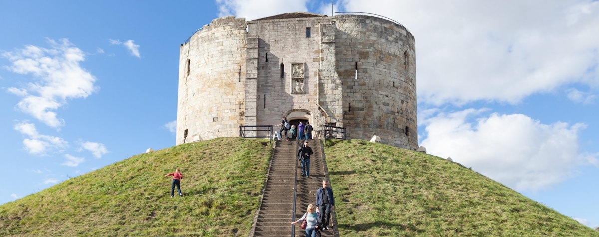York, United Kingdom - October 2, 2016: View of Clifford's Tower, a Norman Motte and Bailey castle in York, England, with visitors climbing the steps to see the attraction.