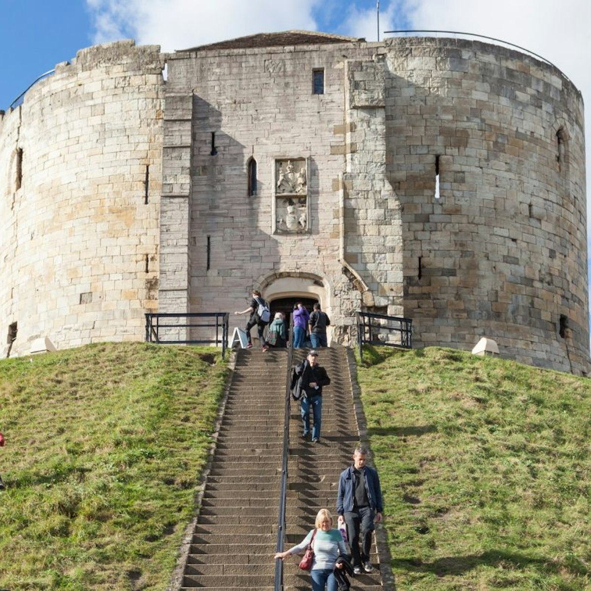 York, United Kingdom - October 2, 2016: View of Clifford's Tower, a Norman Motte and Bailey castle in York, England, with visitors climbing the steps to see the attraction.