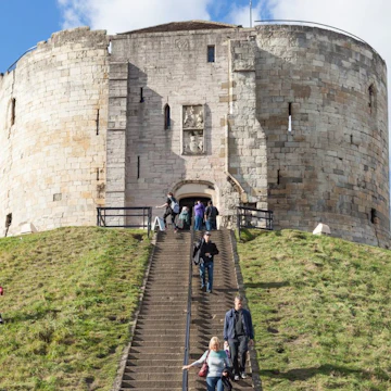 York, United Kingdom - October 2, 2016: View of Clifford's Tower, a Norman Motte and Bailey castle in York, England, with visitors climbing the steps to see the attraction.
