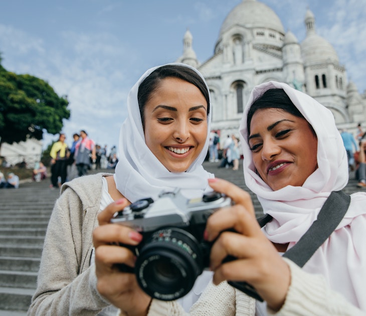 Two smiling Muslim women look at the photos they have taken on their camera whilst stood in front of Montmartre, Paris 