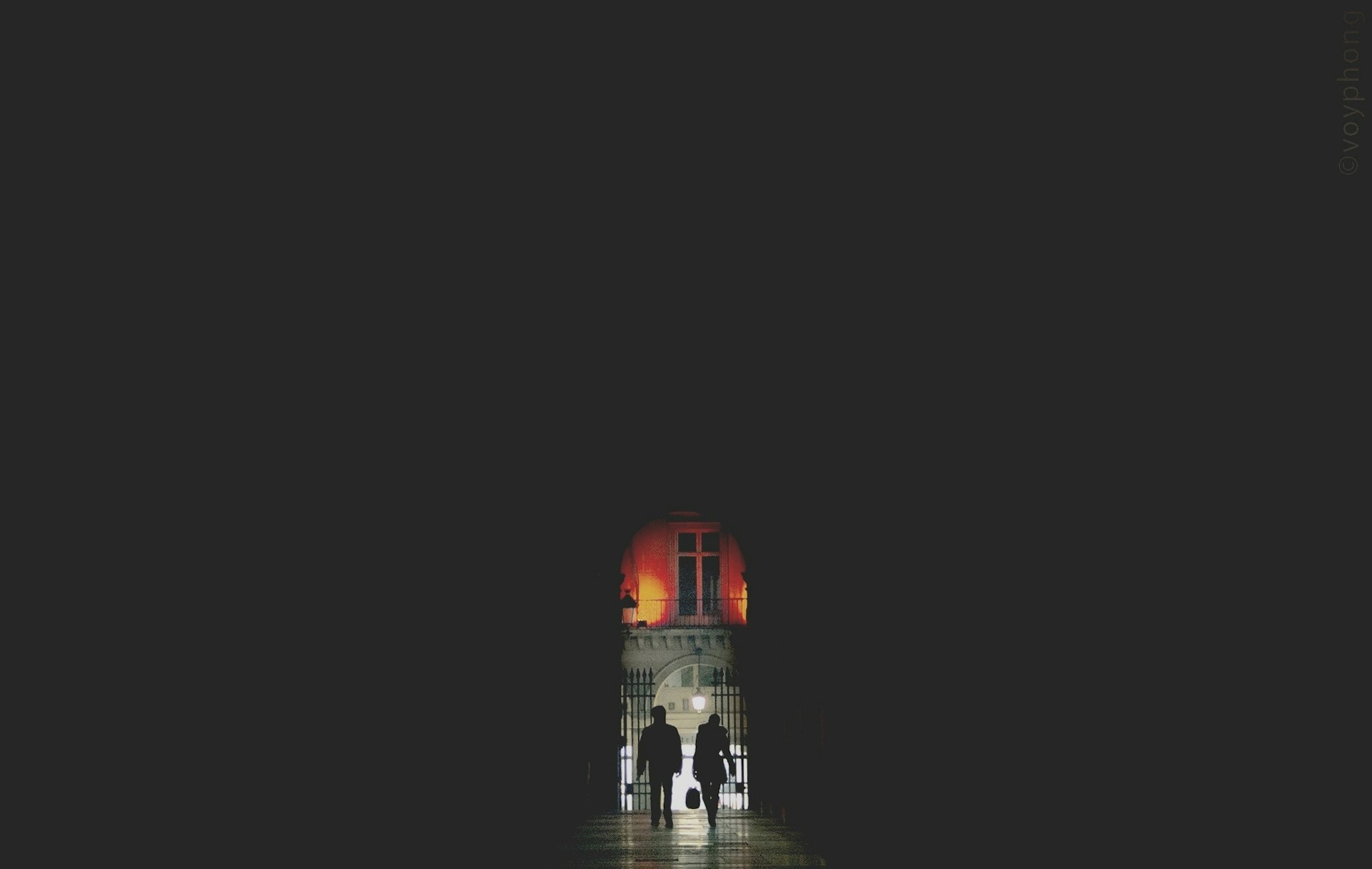 A silhouetted couple walk out of a dark passageway in Paris France and into the night, which is lit up 
