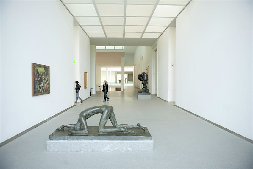 A large hall in an art gallery, with several freestanding sculptures based on the human form.  Two people walk through the exhibition space