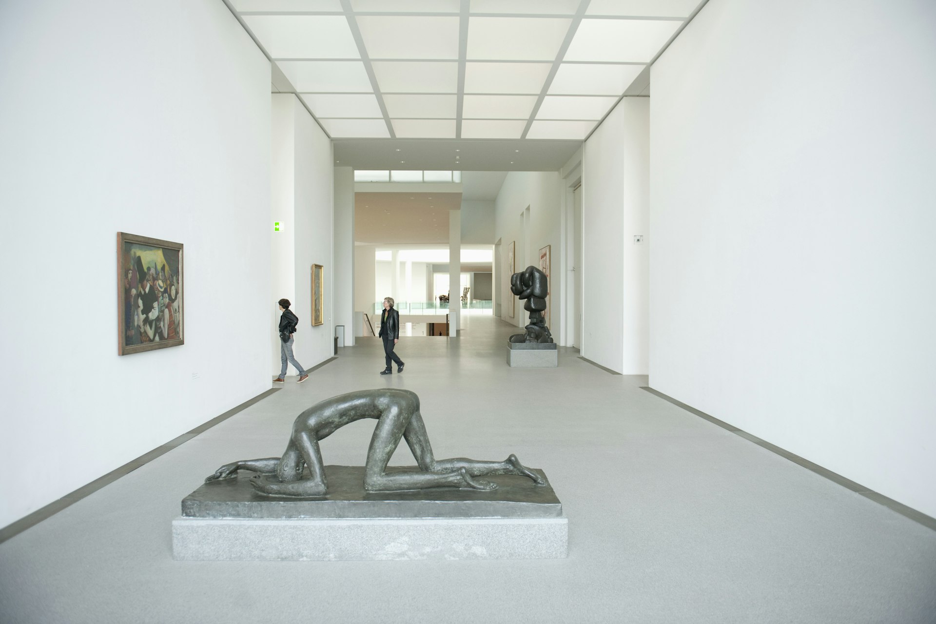 A large hall in an art gallery, with several free-standing sculptures based on the human form. Two people are walking through the exhibition space