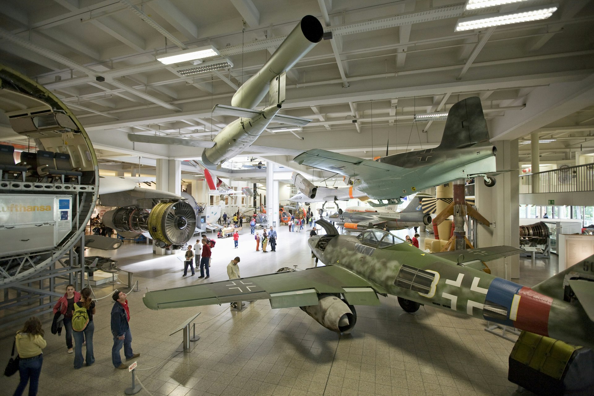 A shot taken from above looking down into a massive museum room furnished with airplanes and other vehicles. People are moving around between the exhibits
