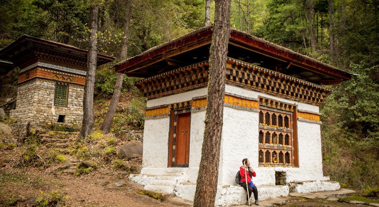 A Woman Outside Tiger's Nest Monastery in Paro, Bhutan Springtime
A young woman, wearing hiking gear, stands outside Tiger's Nest monastery, also known as Paro Taktsang, located 900m up on a cliffside in the valley town of Paro, Bhutan. Tiger's Nest monastery, constructed in 1692, was built around the cave where Guru Rinpoche first meditated. Shot on a bright spring afternoon.