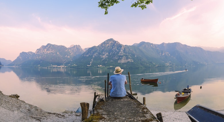 Italy, Lombardy, back view of man sitting on jetty at Lake Idro at morning twilight