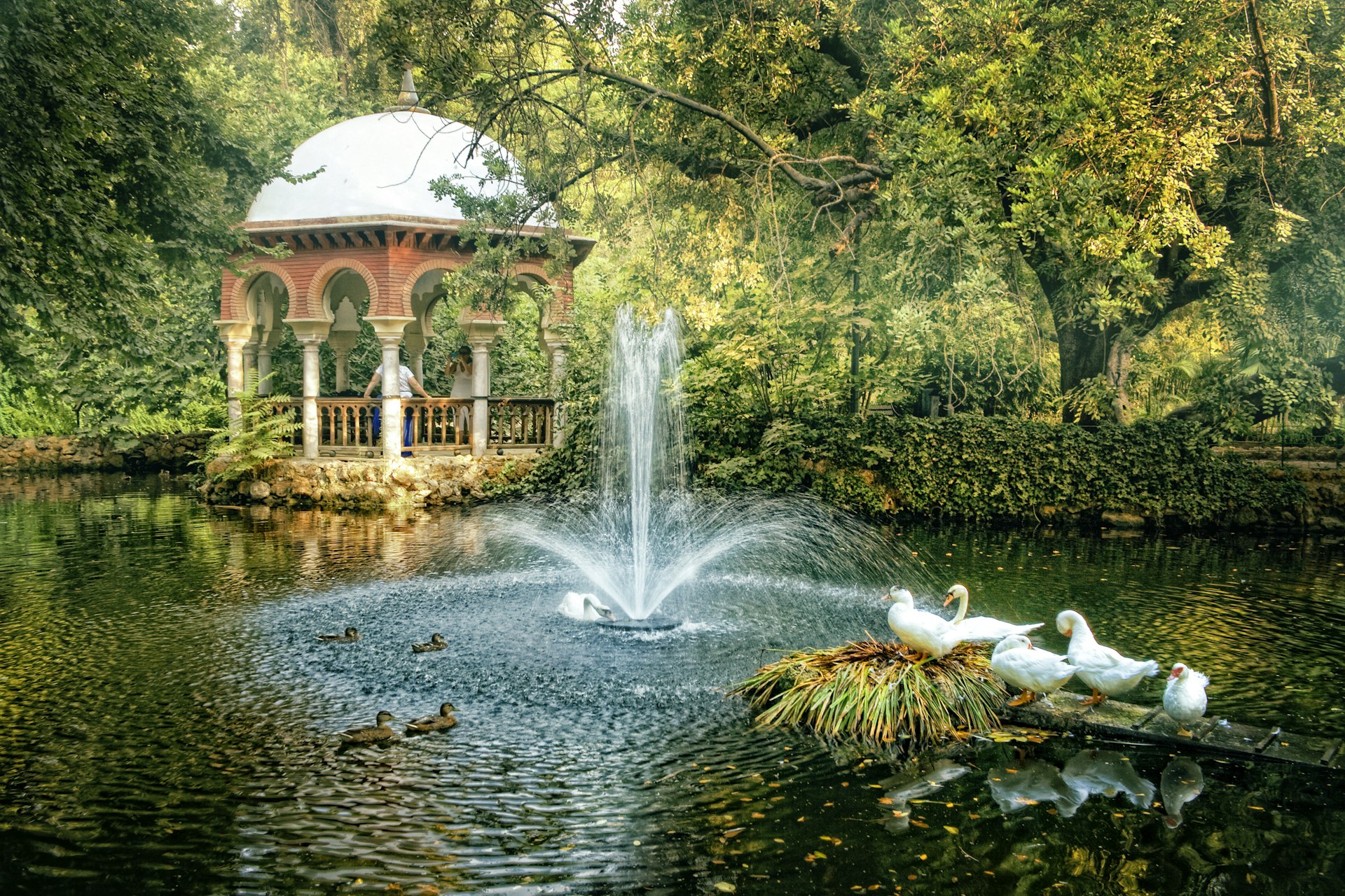 A Moorish-style pavilion by a pond with white ducks at María Luisa Park, Seville, Spain