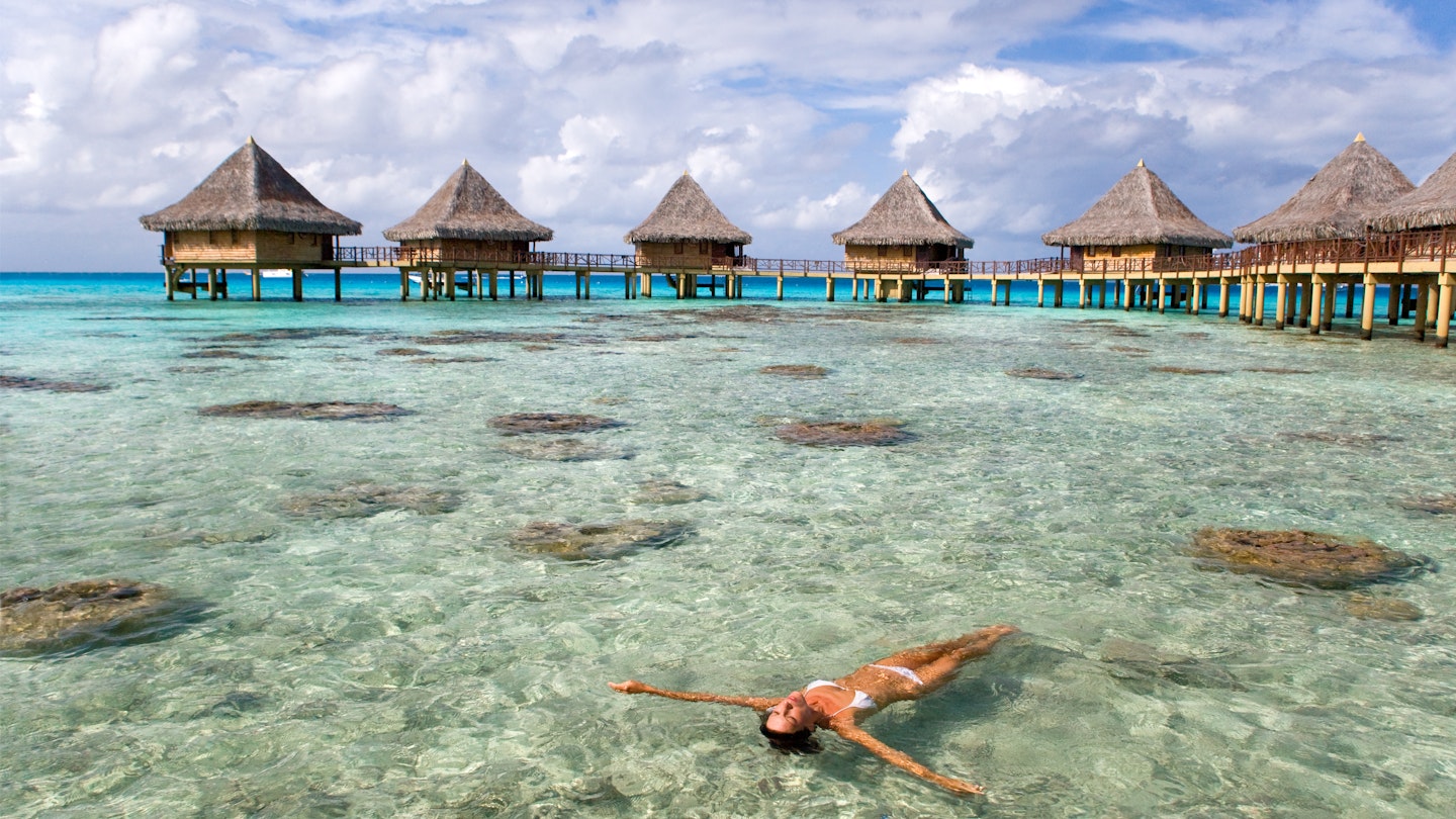 Woman floating and sunbathing near tropical resort bungalows in rangiroa, Tahiti, French Polynesia.