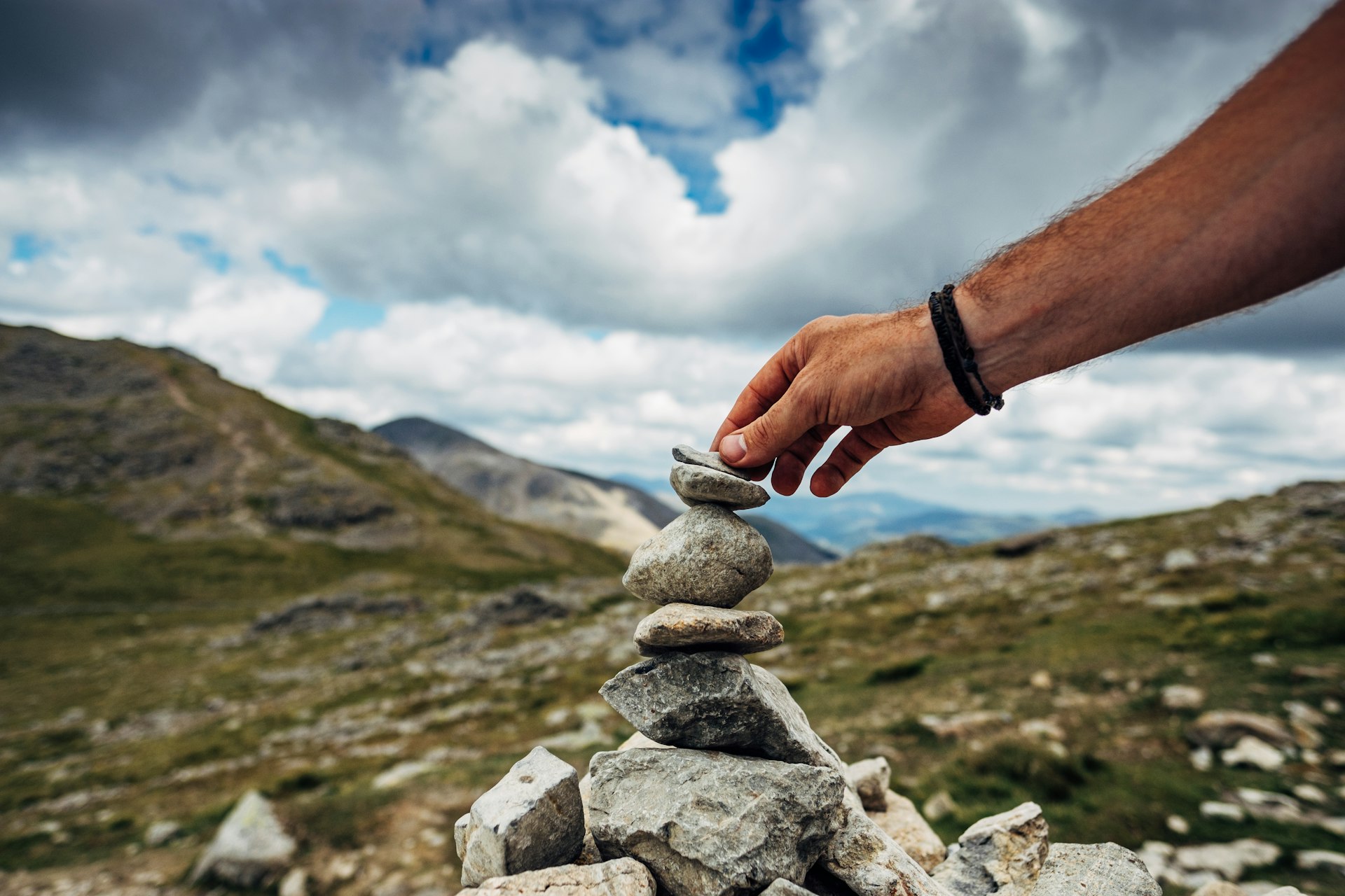 A hand setting a stone atop a cairn stone pile 