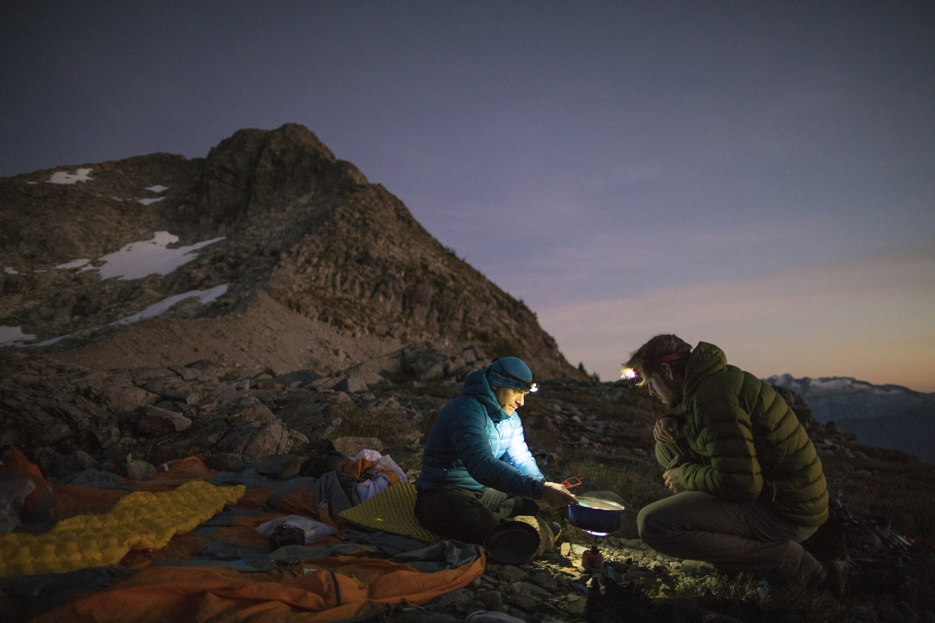Mountaineers cooking on a camp stove and using headlamps after sunset
