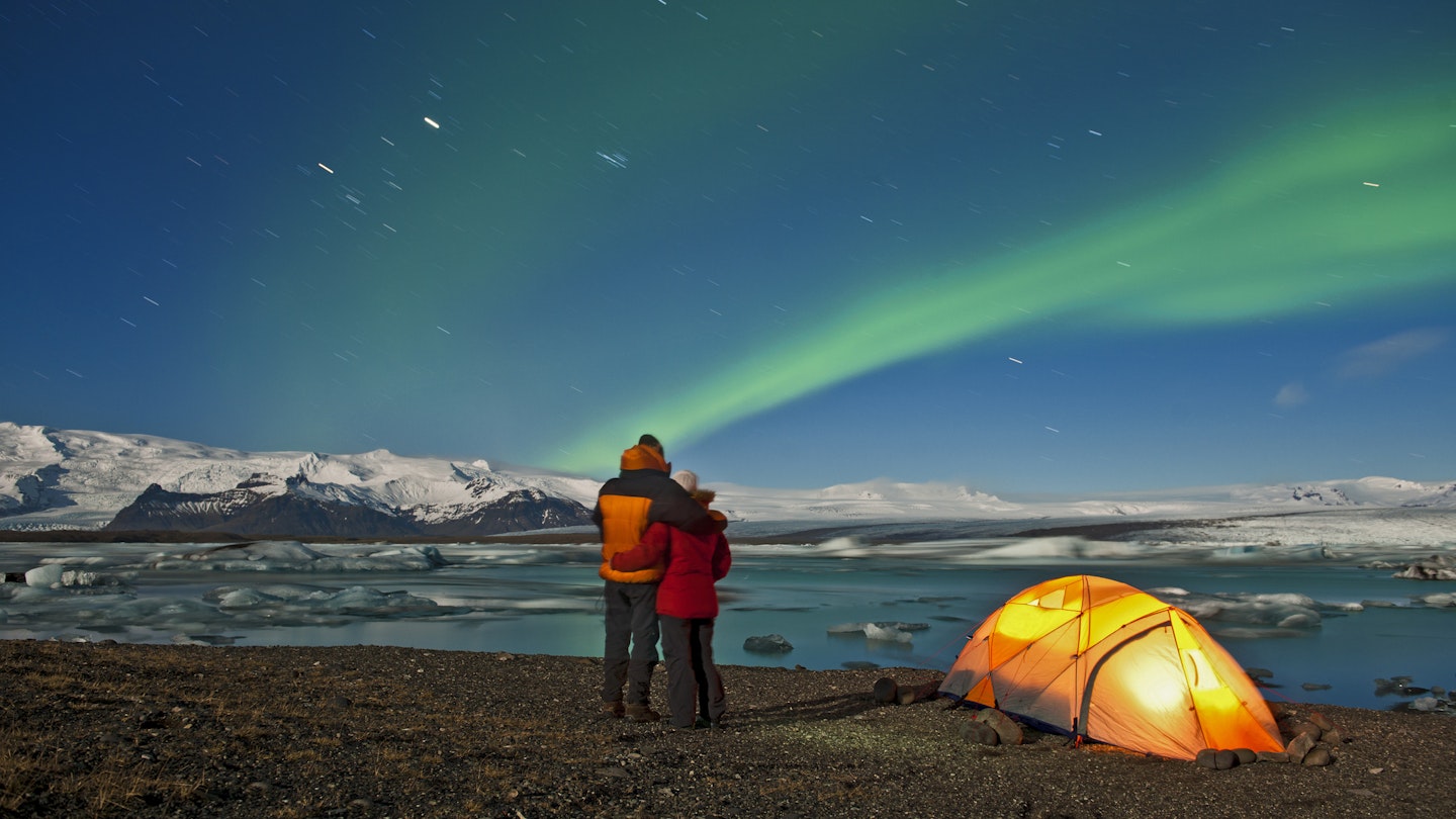 A camping couple gazes out at the northern lights