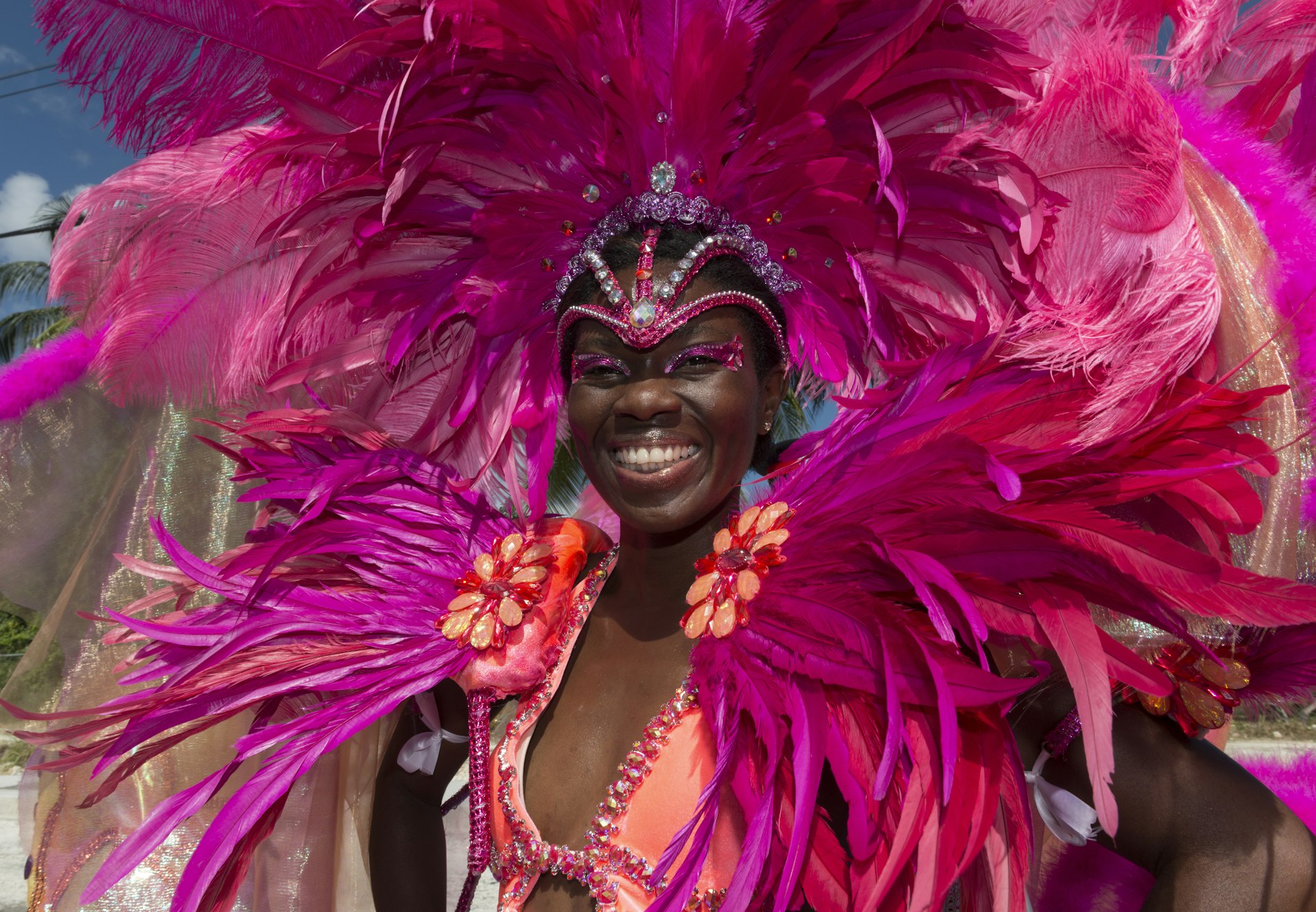 A smiling woman wearing an ornate pink feathered costume during a festival in Barbados