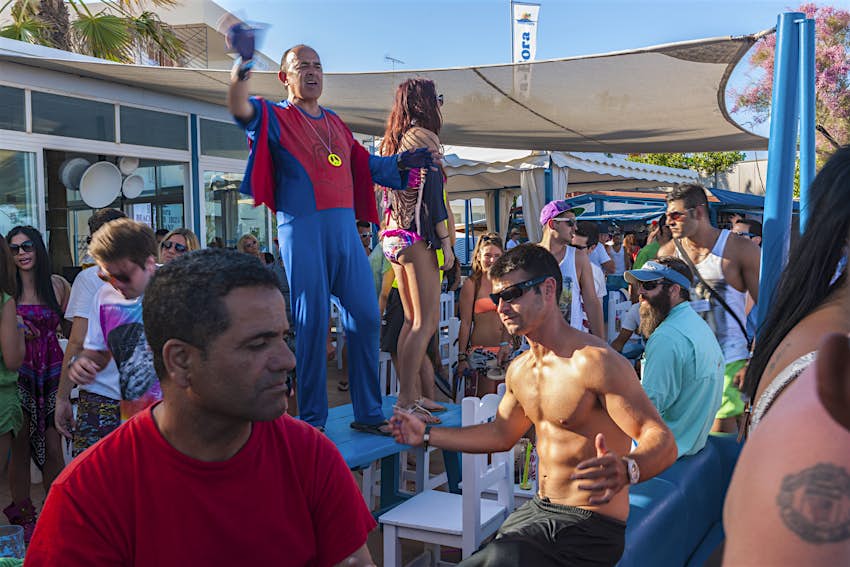 Paplūdimio vakarėlis Platja d'en Bossa, Ibiza, Balearų salos, Ispanija, Viduržemio jūra Vyras Žmogaus-voro apranga, vyras be marškinėlių ir kiti žmonės šoka sausakimšame paplūdimio vakarėlyje Platja d'en Bossa, Ibisoje