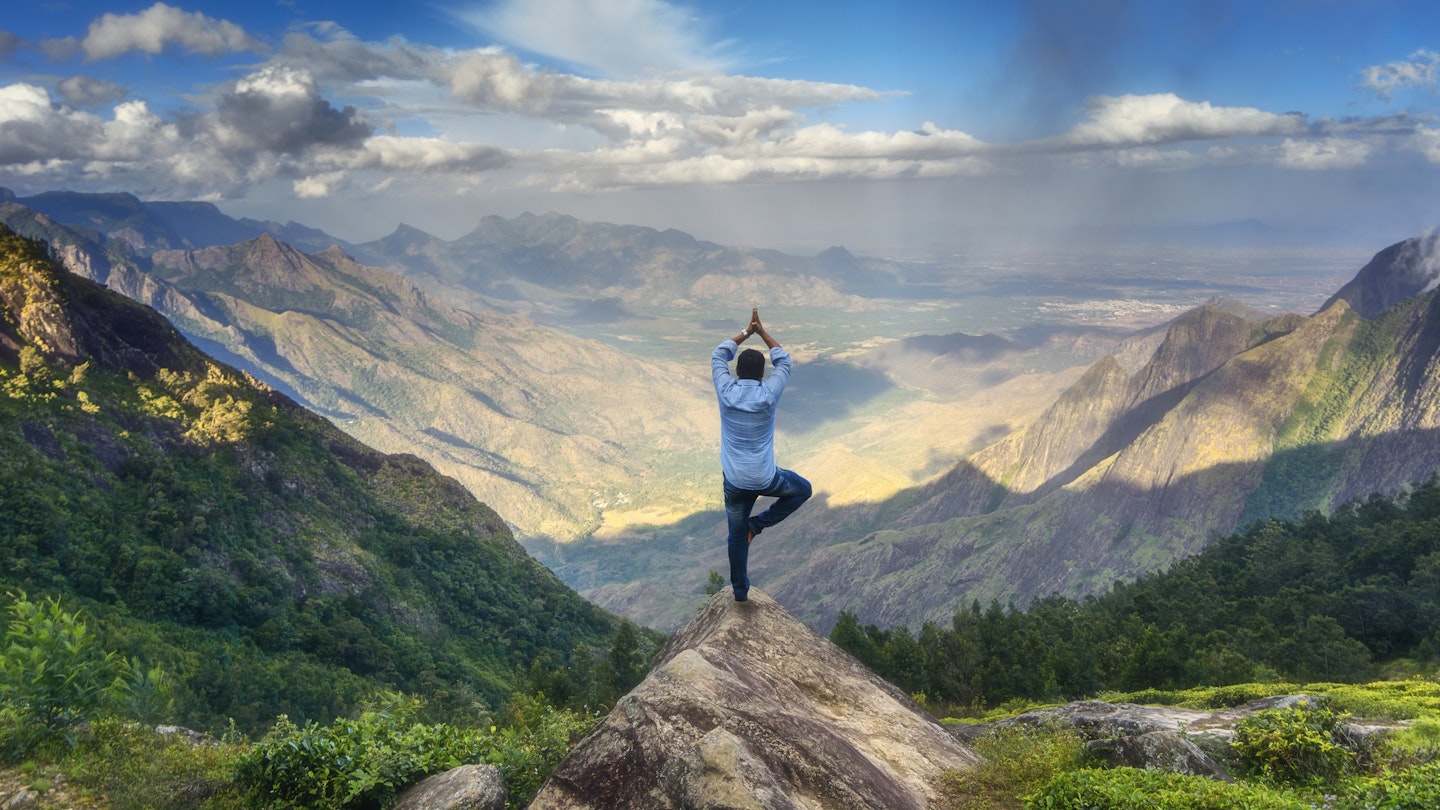 Man doing yoga in front of a mountain view in the Western Ghats