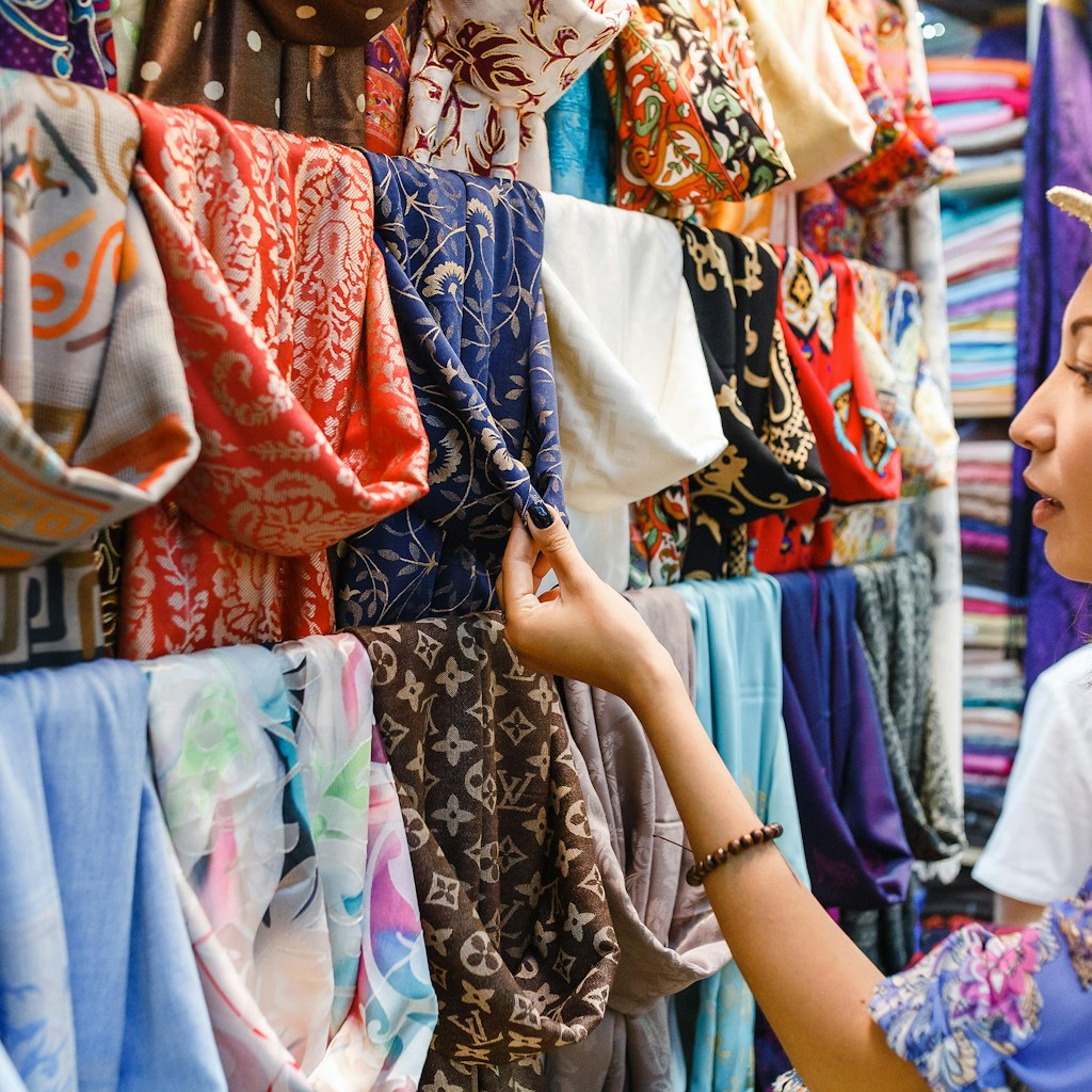 Young woman shopping for a new scarf and choosing colourful fabric in a bazar.