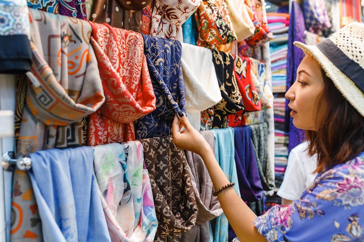 Young woman shopping for a new scarf and choosing colourful fabric in a bazar.