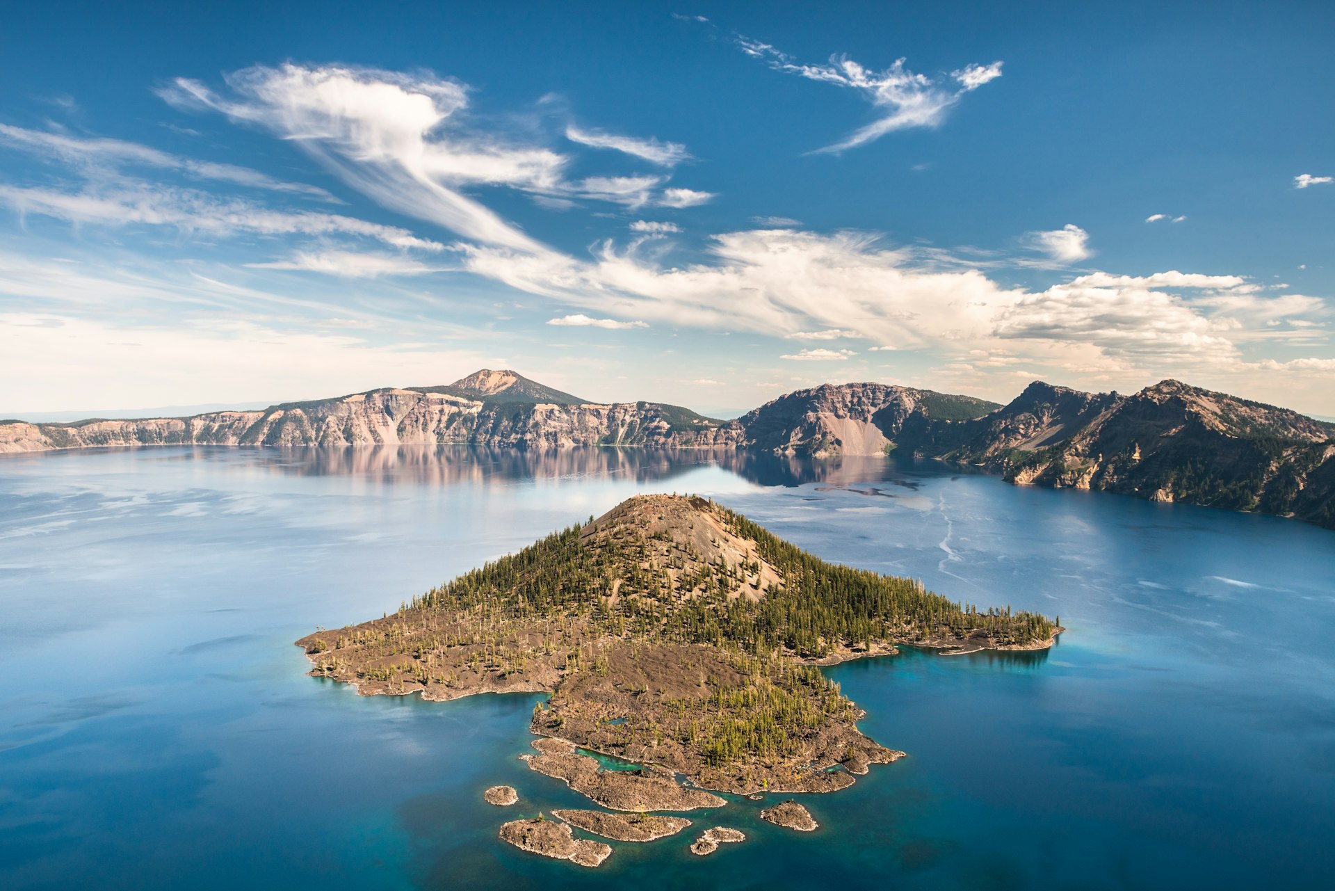 The tree-covered Wizard Island in Crater Lake, at Crater Lake National Park on a bright, blue sky day