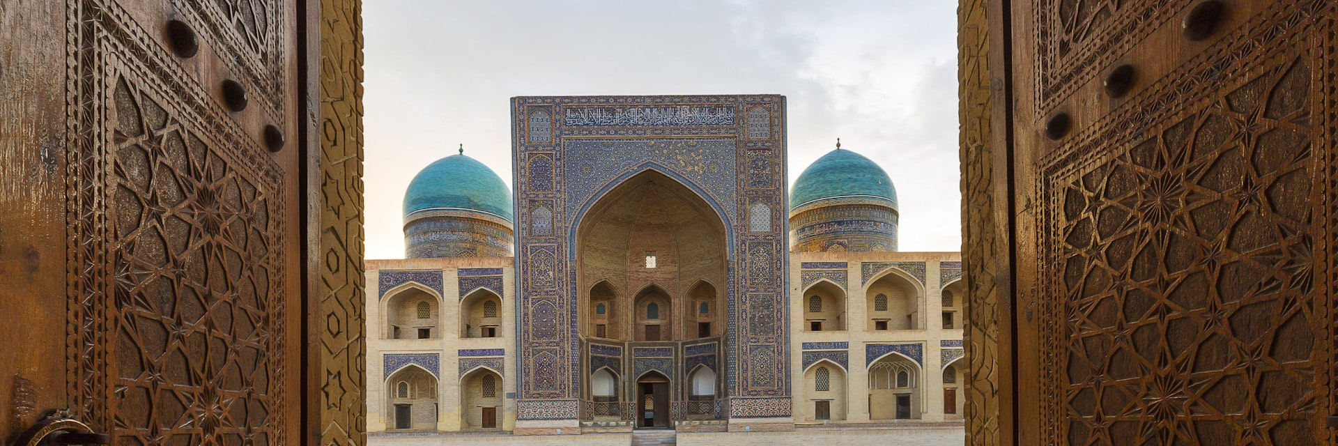 Blue domes of the Madressa through open wooden door in Bukhara, Uzbekistan.