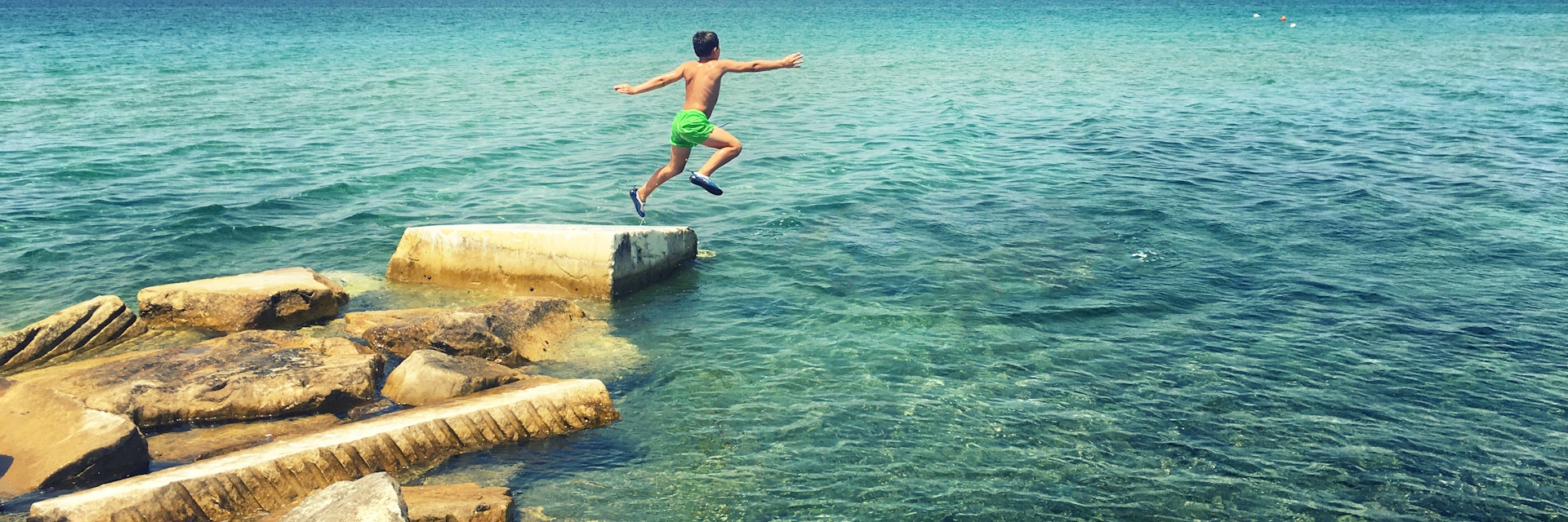 Boy jumping off rocks into the sea.