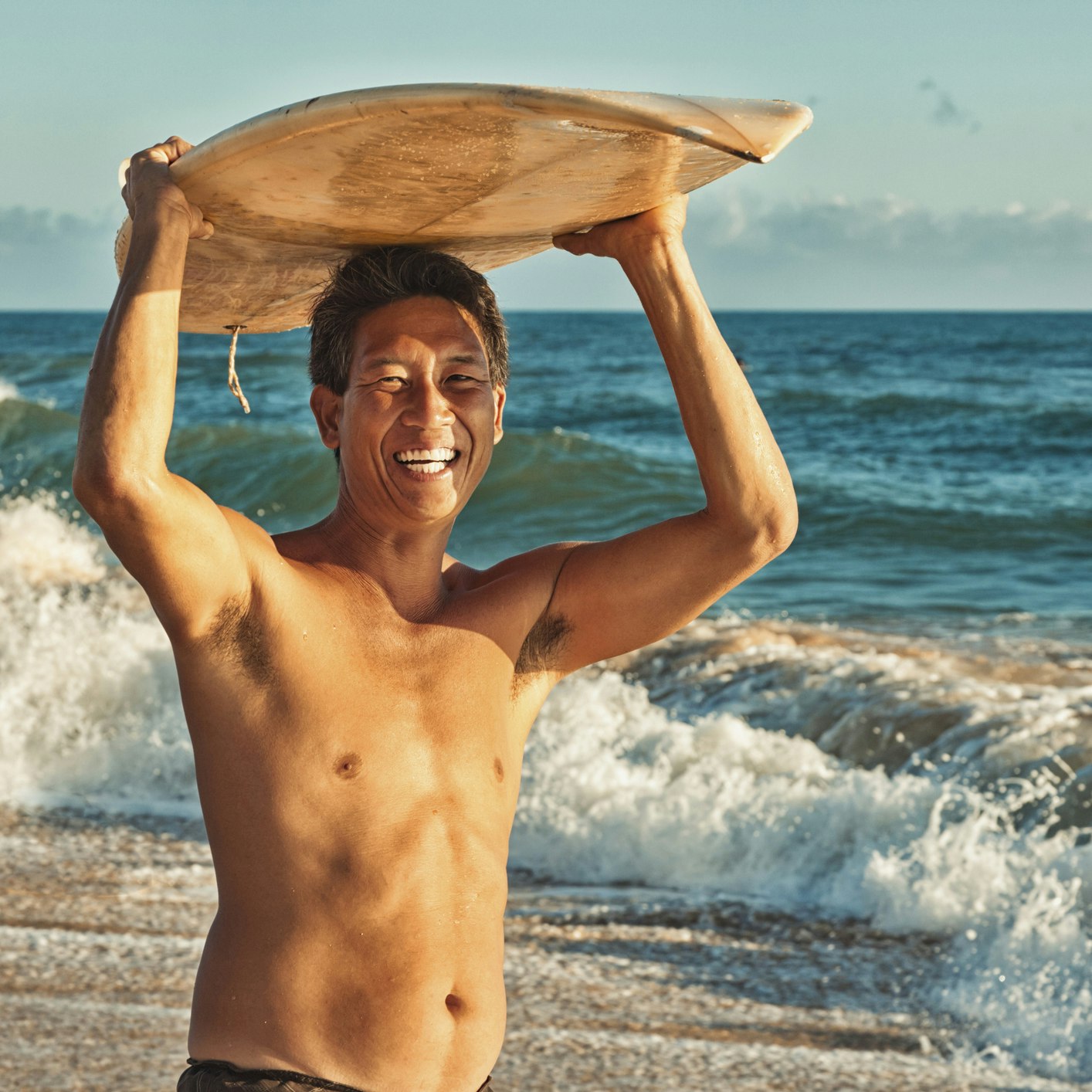 "Photo of a local Hawaiian surfer standing with his surf board over-head; Kauai, HI."