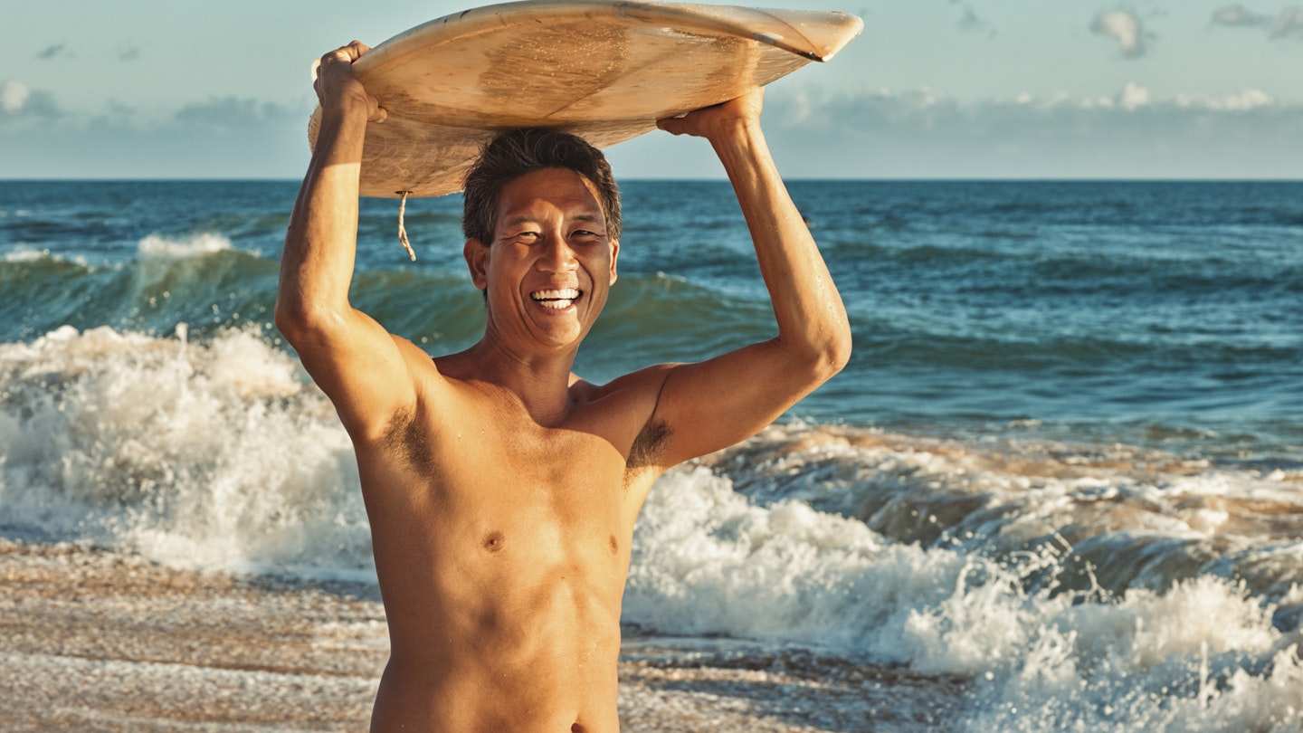 "Photo of a local Hawaiian surfer standing with his surf board over-head; Kauai, HI."