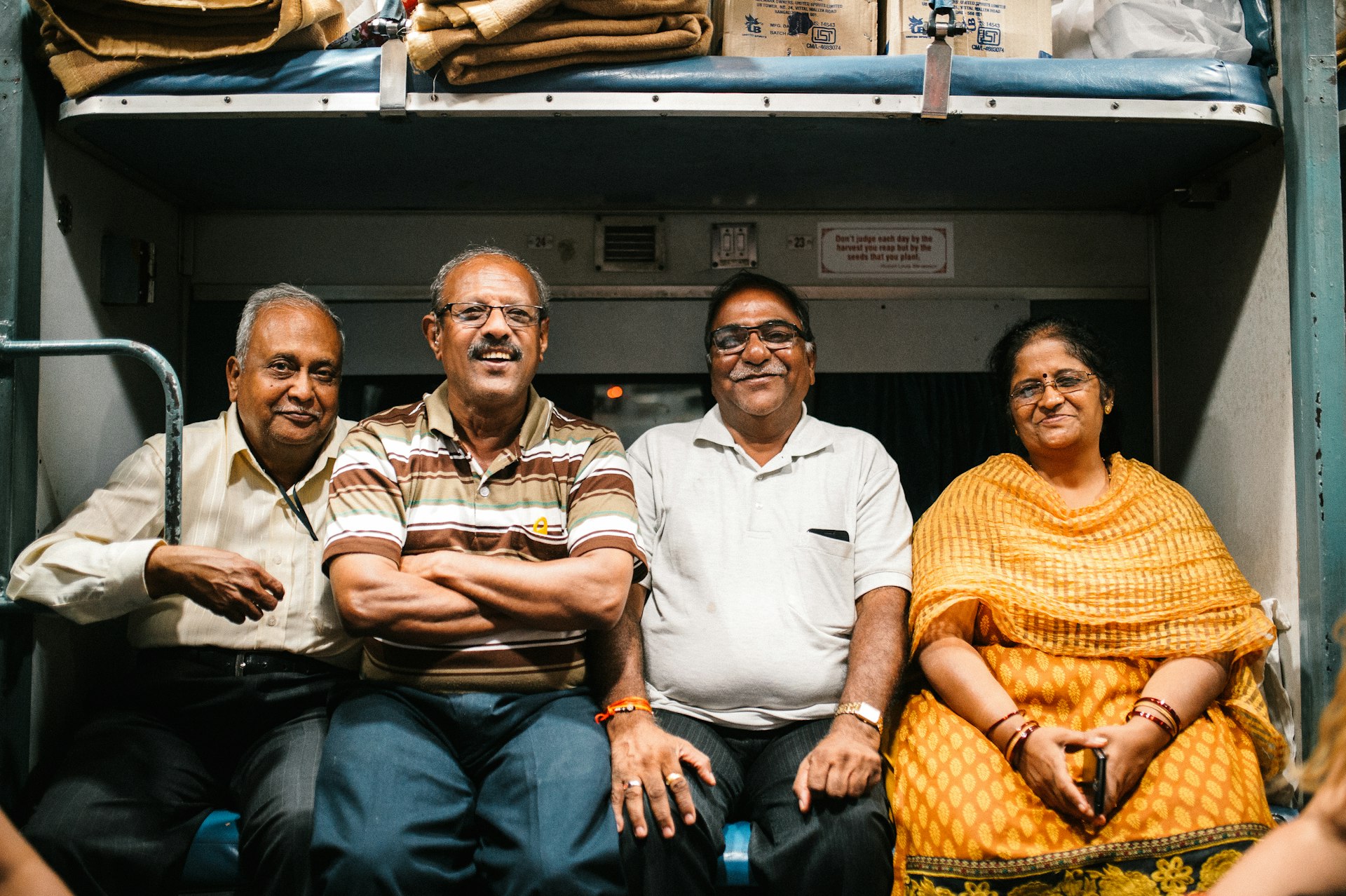 A group of four Indian travelers cram together on a bench on a train and smile at the camera
