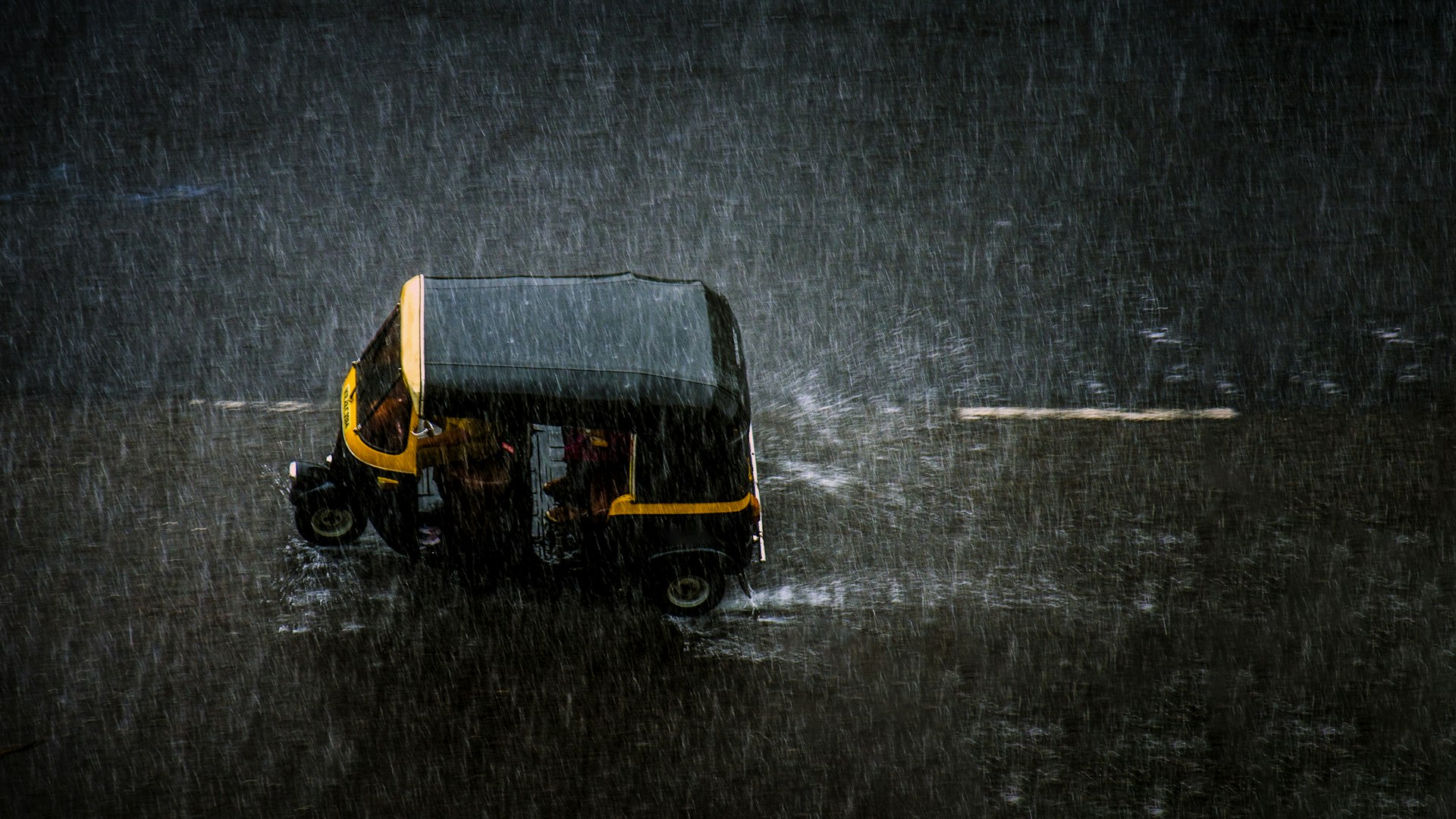 An auto rickshaw shot from above on the road during a heavy rainfall