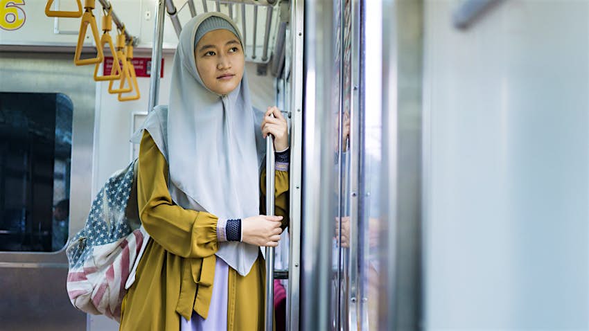 Wanita Muslim muda mengenakan jilbab dan ransel berdiri di depan pintu kereta api di Jakarta, Indonesia