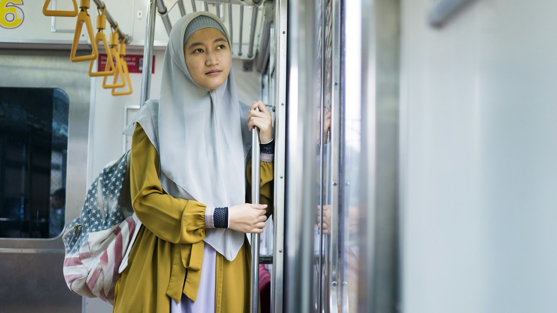Young Muslim woman wearing hijab and backpack standing in front of the door of a train in Jakarta, Indonesia