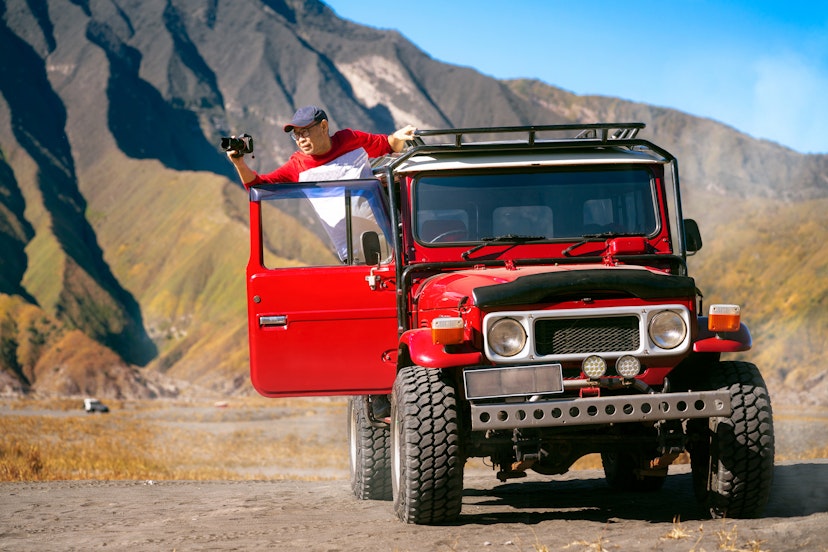 Traveller sit and take a photo on a vintage off road car with Bromo mountain background, Java island, Indonesia, this photo can use for travel, holiday and outdoor concept