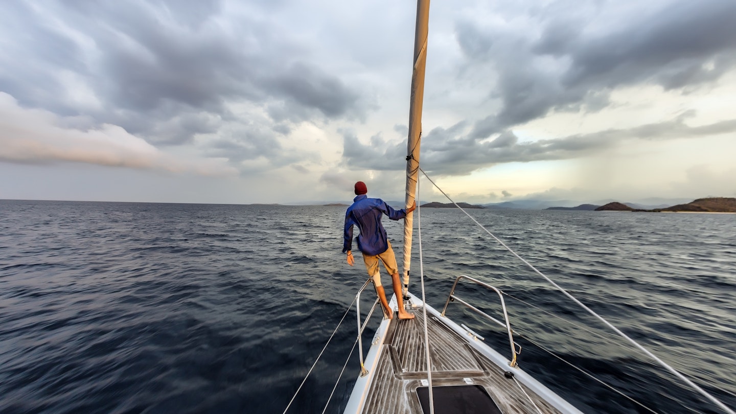 Rear view shot of single white man standing on bow of yacht looking out across Lombok, Indonesia