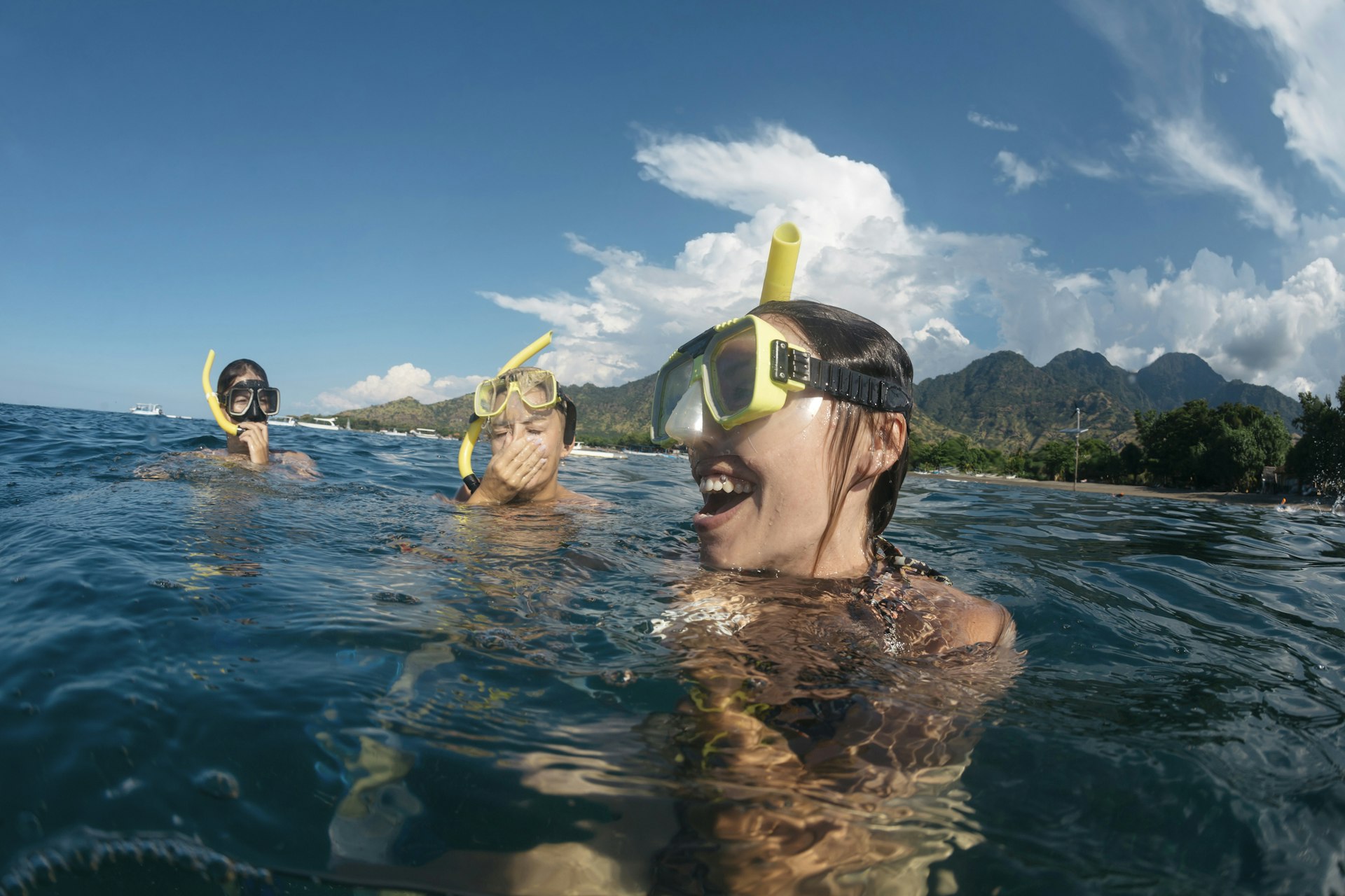 Three women on the surface if the water wearing snorkeling gear and laughing