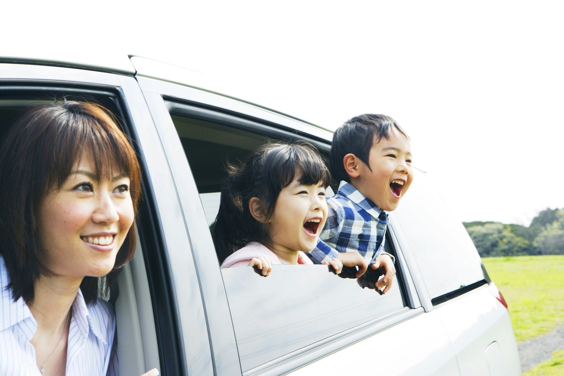 Excited Japanese family - a mother and two young kids - smile and cheer from a car window in rural Japan on a sunny day