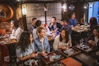 Wide angle view of Mongolian, Japanese, and Caucasian women sitting at sushi bar and other patrons in Tokyo izakaya.