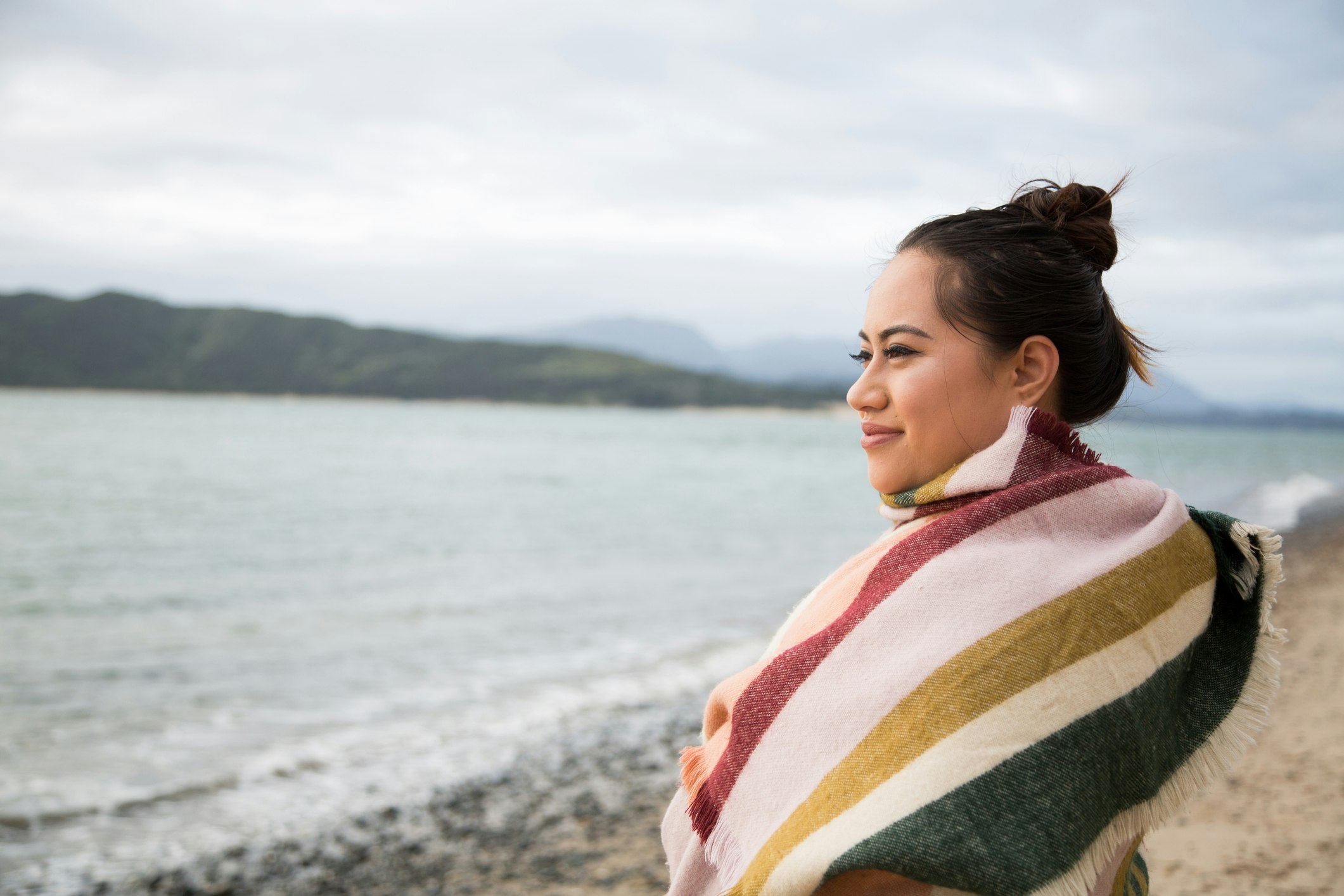 Maori woman wrapped in a shawl looks out to sea on a beautiful beach