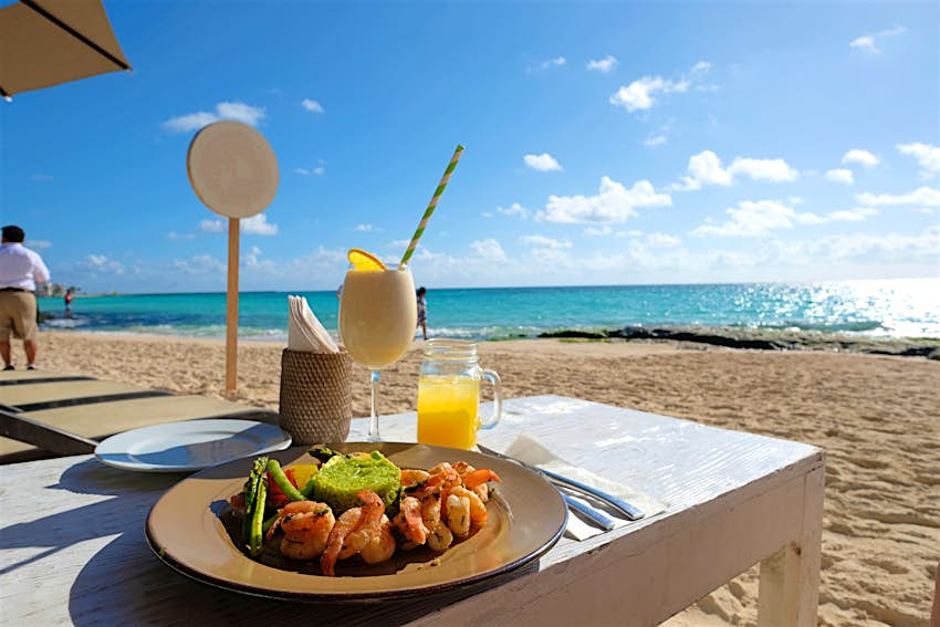 A shot of a cocktail and a plate of seafood on a table at a sandy beach