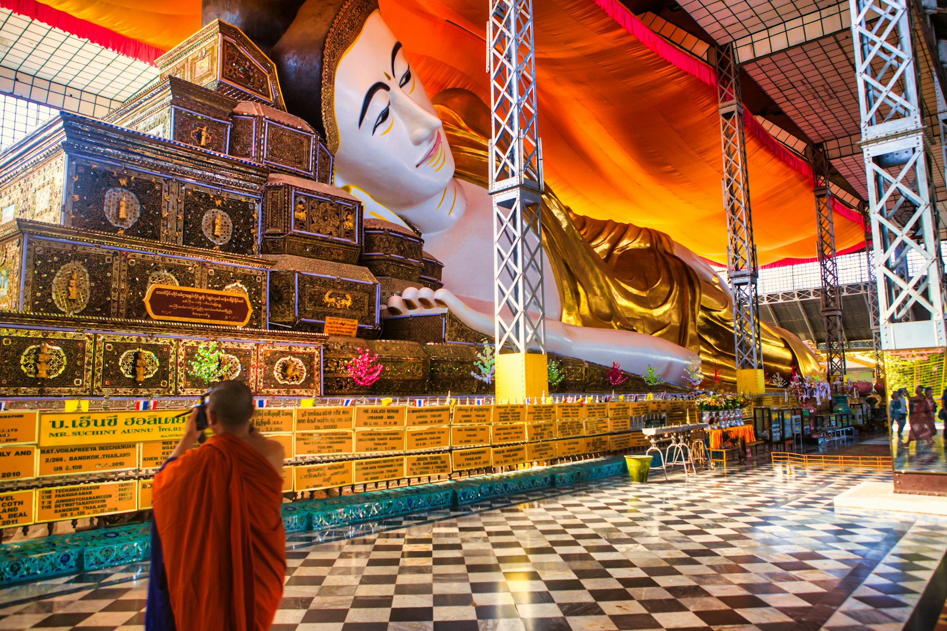A monk wearing orange robes takes a photograph of a huge reclining Buddha
