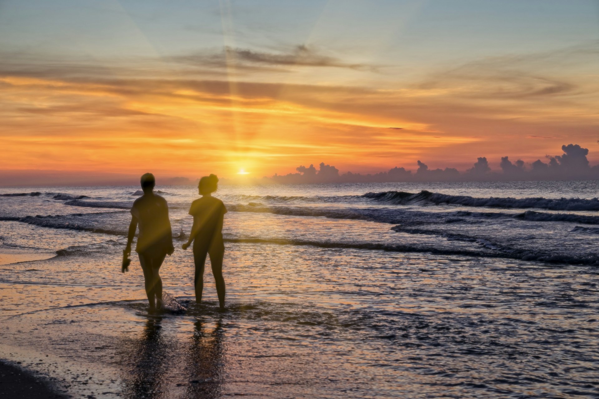 Two people walk through the shallow waters of Myrtle Beach during sun rise.
