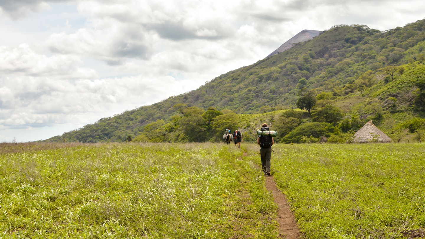 San Jacinto, Nicaragua - June 18, 2015: Group of hikers walks through the field and is about to ascend the slopes of the very active Telica volcano in San Jacinto, Leon, Nicaragua. Central America
